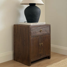 Load image into Gallery viewer, Wooden nightstand with a lamp and books against a beige wall