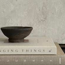 Load image into Gallery viewer, A dark brown rustic ceramic bowl sits on top of a cream-colored book, which is stacked on another book against a textured light canvas art 
