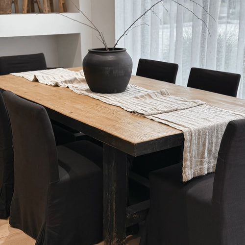 Dining table with a black vase and patterned tablecloth, surrounded by black chairs.