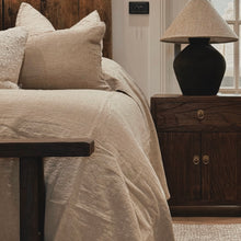 Load image into Gallery viewer, Bedroom with beige bedding, brown bedsides, wooden headboard and nightstand with lamp.
